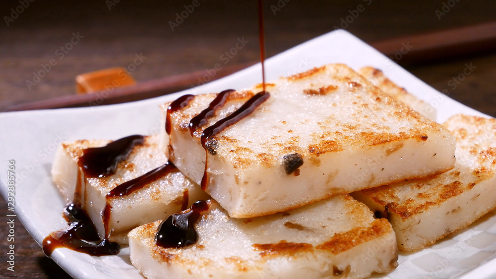 Pouring black soy sauce on ready-to-eat delicious turnip cake, Chinese traditional local dish radish