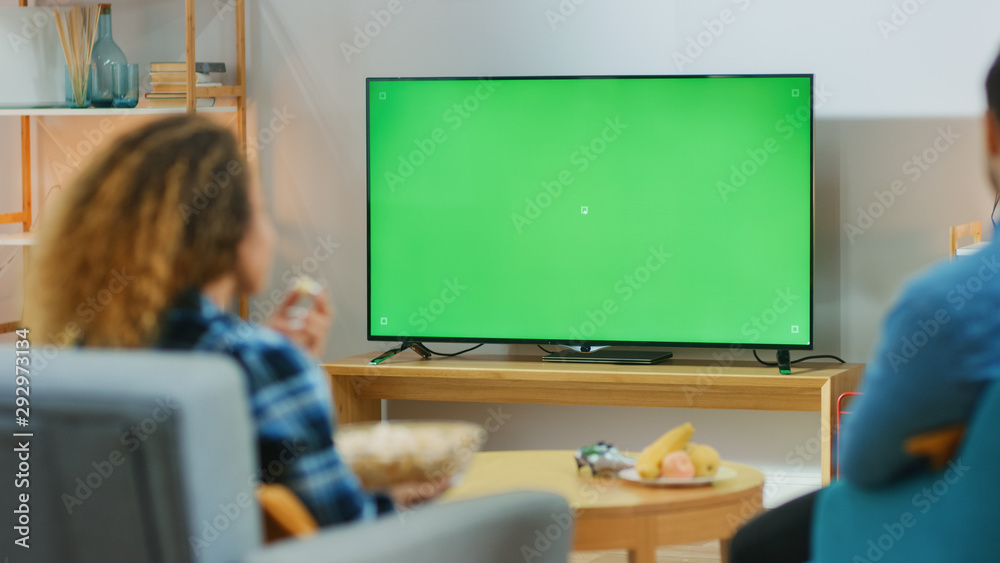 幸福的一对情侣坐在家里的客厅里看绿色Chroma键屏电视，在C上放松