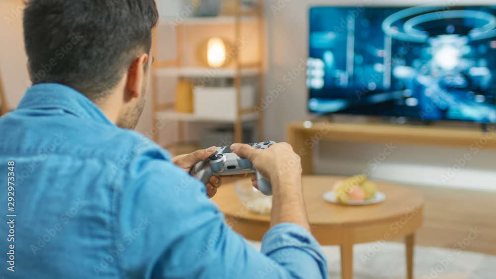 在客厅里，一个坐在沙发上的男人拿着控制器在控制台上玩电子游戏，3D Actio