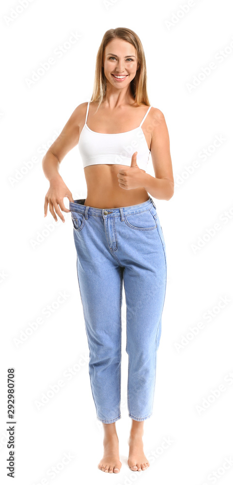 穿着宽松牛仔裤的漂亮年轻女子在白色背景上竖起大拇指。减肥概念