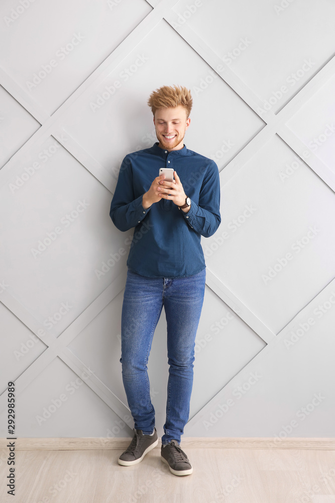 Portrait of young man with mobile phone near grey wall