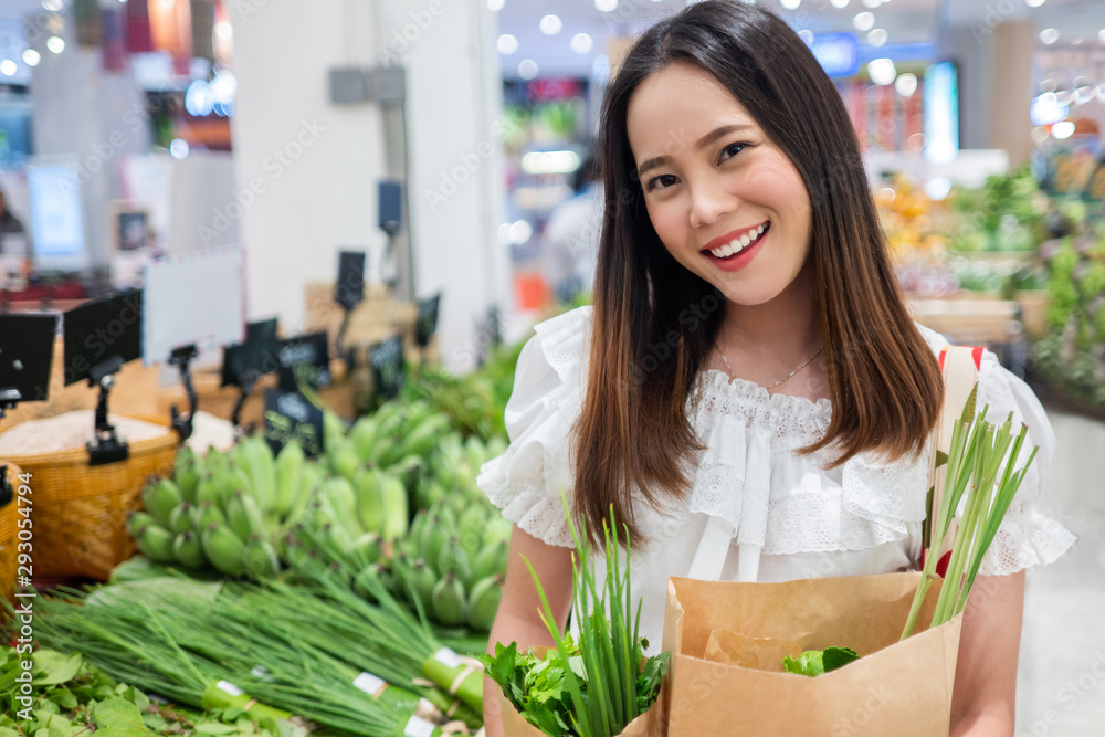 亚洲妇女在超市买蔬菜。她用纸袋和编织袋。为了环境