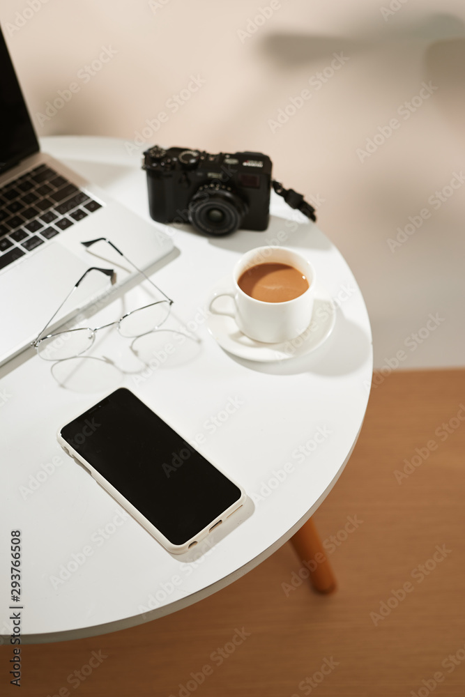 带咖啡杯、笔记本电脑、相机、智能手机和眼镜的办公桌俯视图