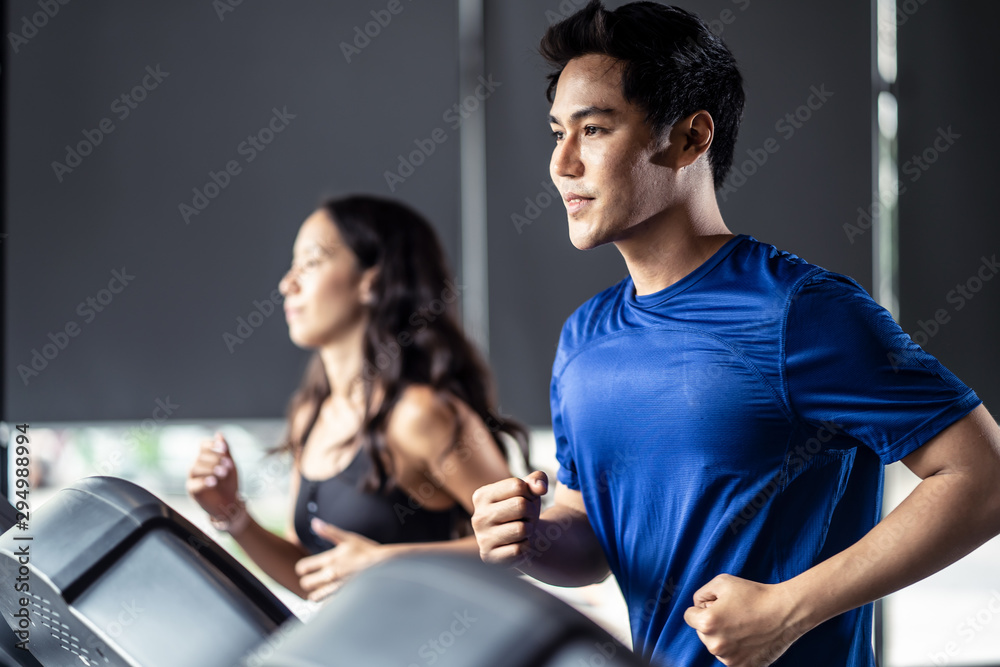 Young fit handsome Asian man and beautiful Asian woman running on treadmill or running machine in mo