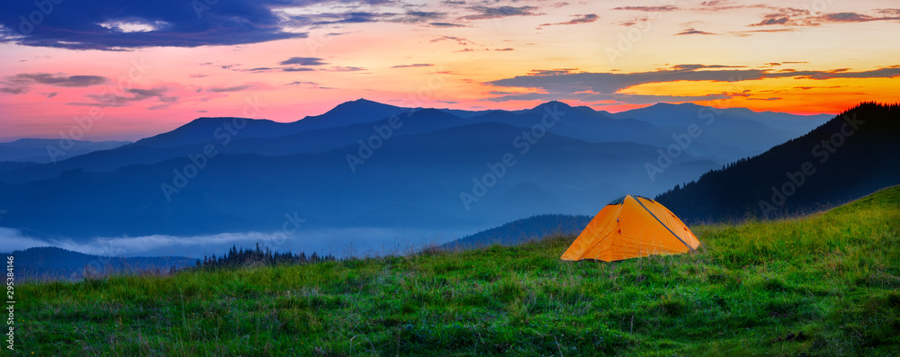 日落时山上的橙色帐篷