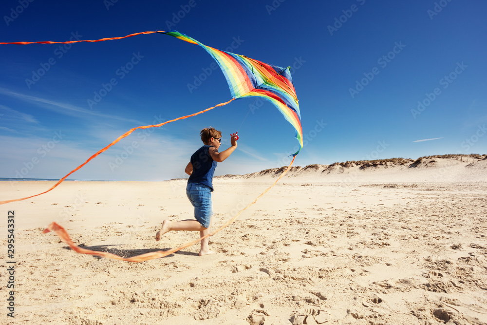 男孩带着彩条风筝在沙滩上奔跑
