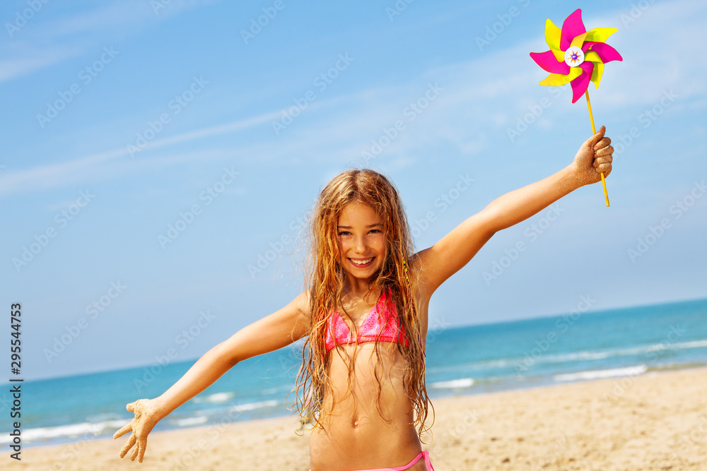 快乐女孩穿着比基尼在海滩上微笑，带着风车