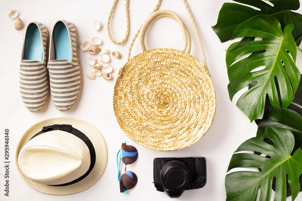 Straw hat, camera, bag, summer shoes, sunglasses, shells and tropical leaves over white background, 