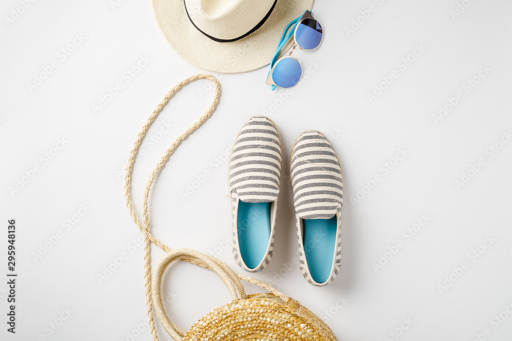 白色背景平躺旅行者配饰，搭配草帽、夏季鞋、包包和太阳镜。