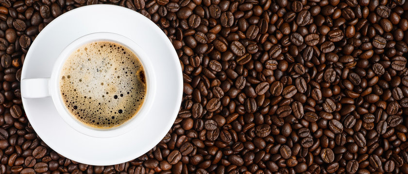 panoramic coffee background of a cup of black coffee covered with coffee bubble on roasted arabica coffee beans