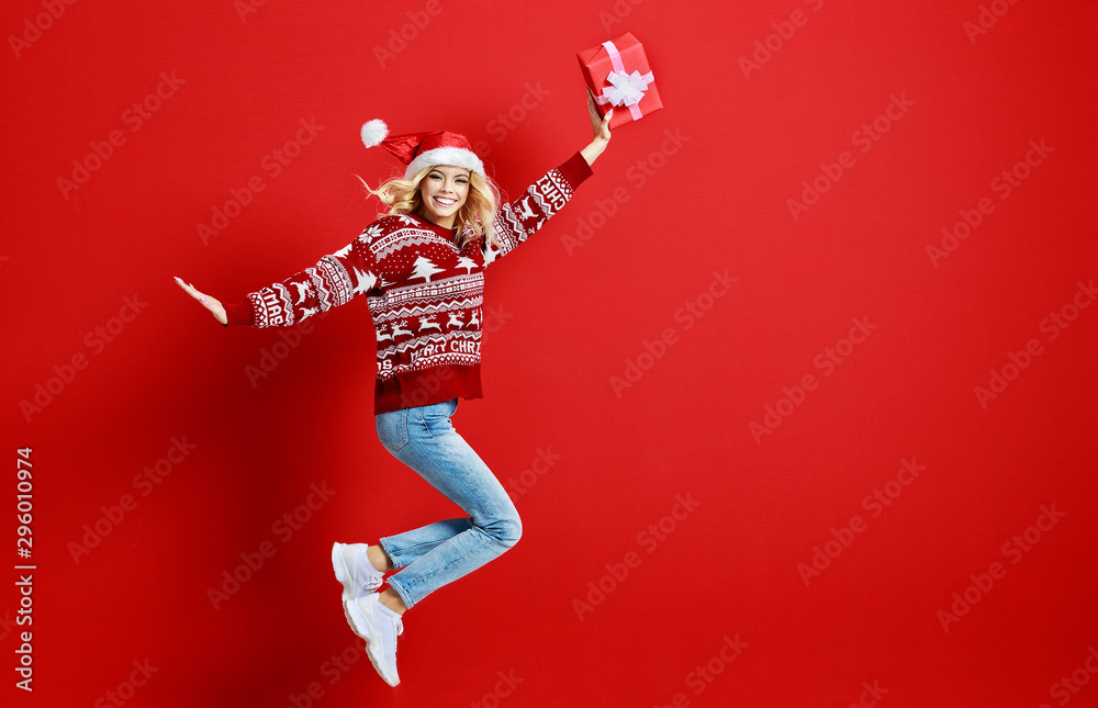 快乐快乐的年轻女孩戴着圣诞帽，红底礼物，笑着跳起来