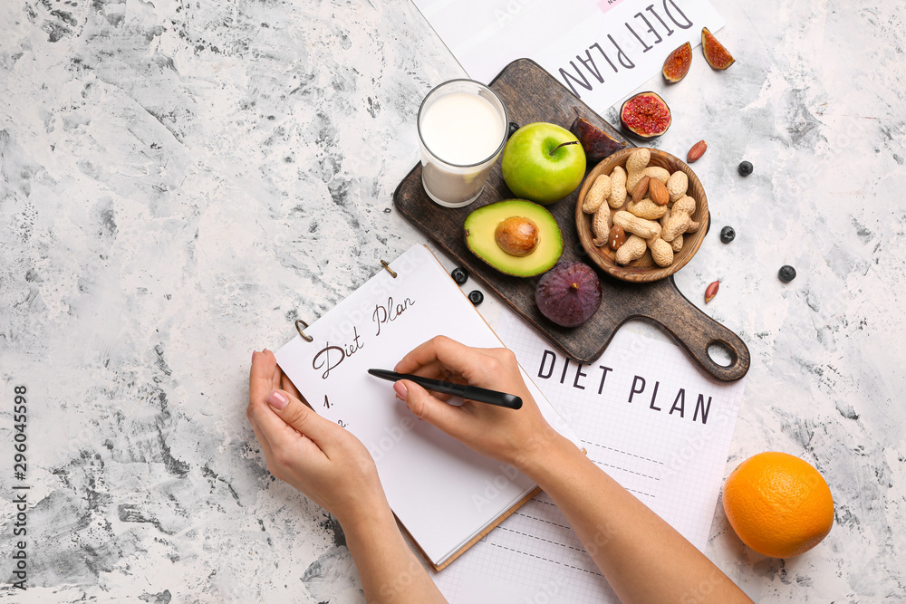 女人在笔记本上写东西，在白色桌子上写健康产品。饮食概念