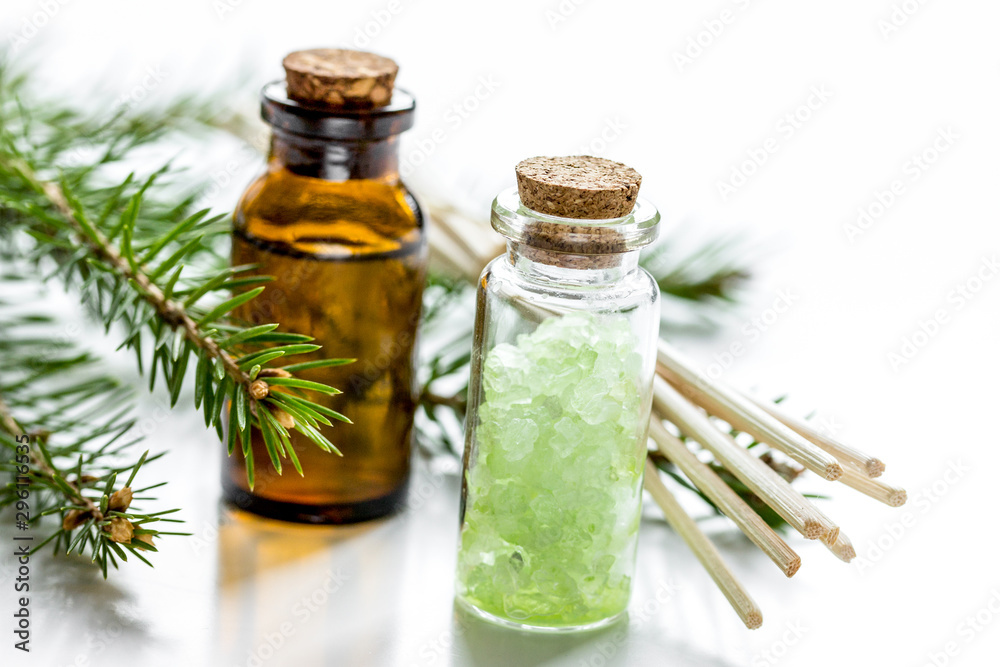 白色桌子背景上装在瓶子里的云杉针芳香疗法精油和盐