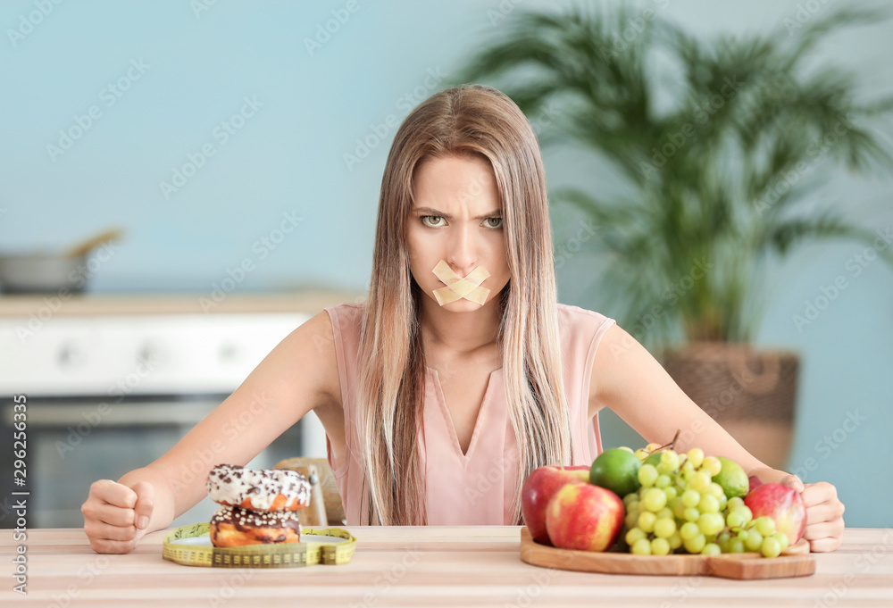愤怒的女人，嘴巴被胶带封住，厨房里有健康和不健康的食物。饮食概念