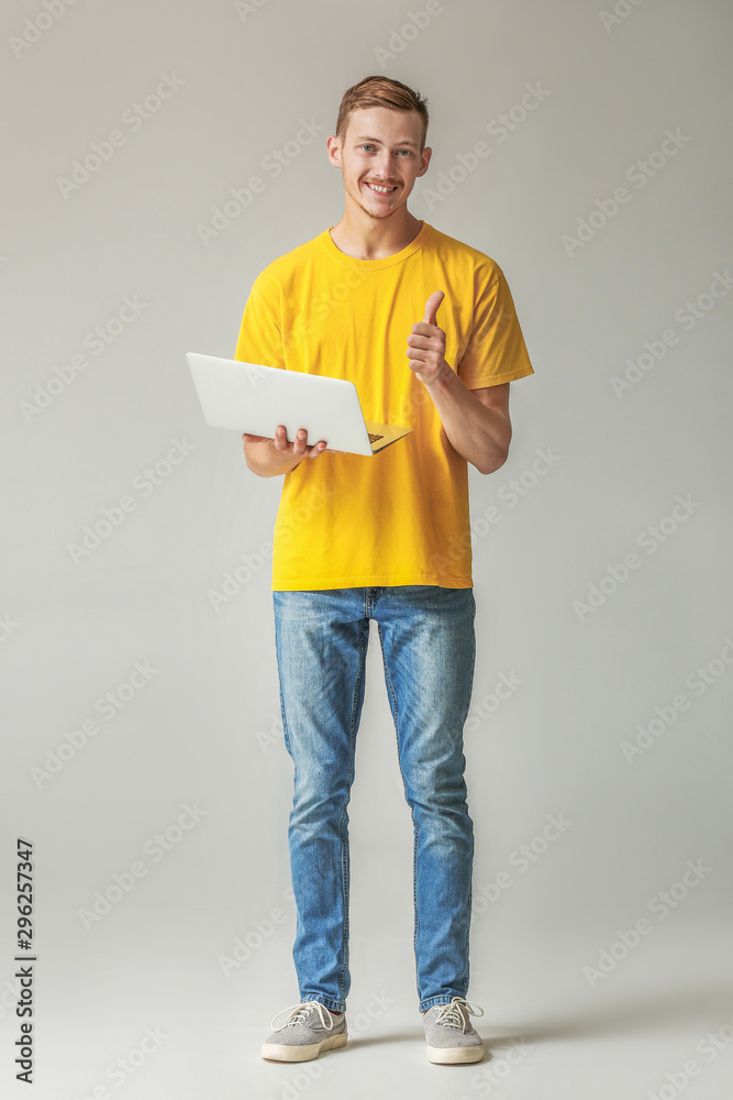 年轻人穿着时尚t恤，笔记本电脑在灰色背景下显示拇指向上的手势