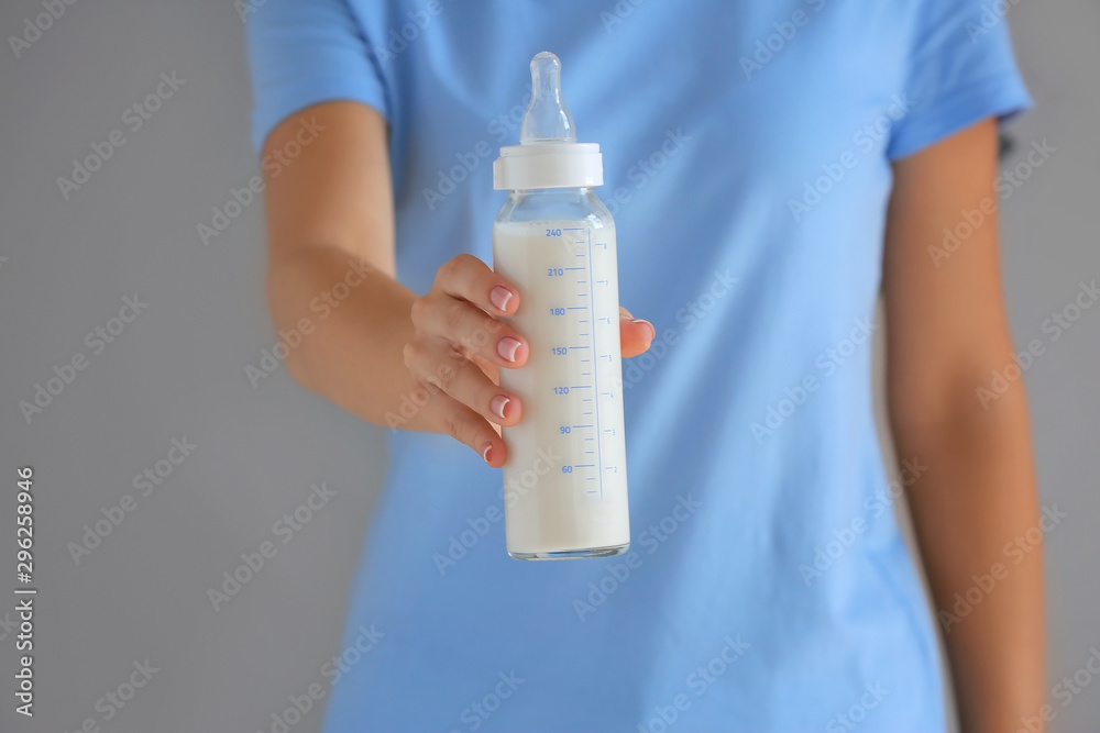 母亲拿着一瓶灰色背景的婴儿配方奶粉，特写