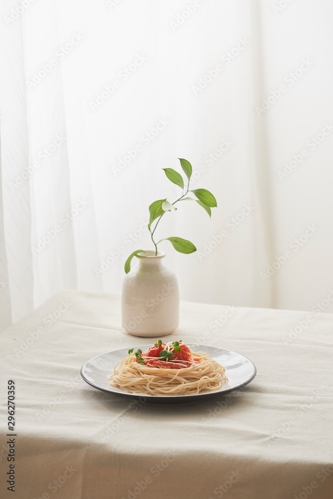 食物，白盘子里的意大利肉酱意大利面和白桌子上的一瓶植物