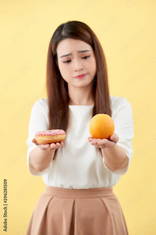 拿着甜甜圈和橙色的年轻女子被隔离在黄色背景上