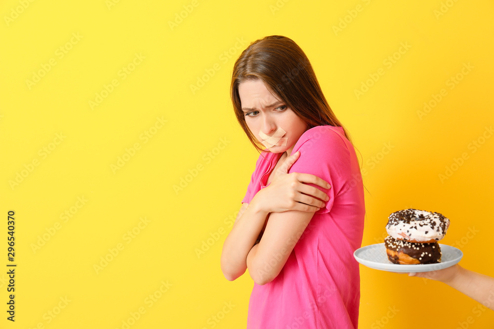 向悲伤的女人献上彩色背景的美味甜甜圈。饮食理念