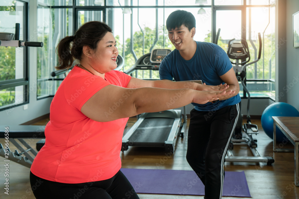 两名亚洲教练男子和超重女子在现代健身房一起锻炼伸展运动，快乐而微笑