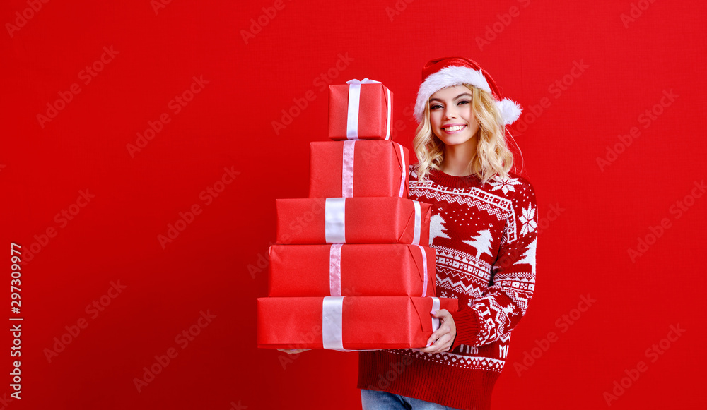 快乐的年轻开朗的女孩戴着圣诞帽，拿着红底礼物，笑着跳了起来。