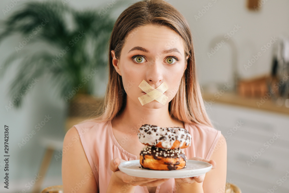 压力重重的女人，嘴巴被胶带封住，厨房里有美味的甜甜圈。饮食概念