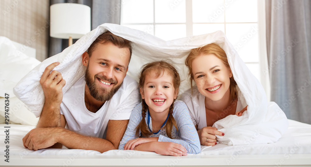 幸福的家庭母亲，父亲和孩子在家里的床上大笑、玩耍和微笑。