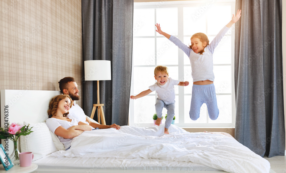幸福的家庭妈妈、爸爸和孩子在家里的床上欢笑、玩耍和跳跃