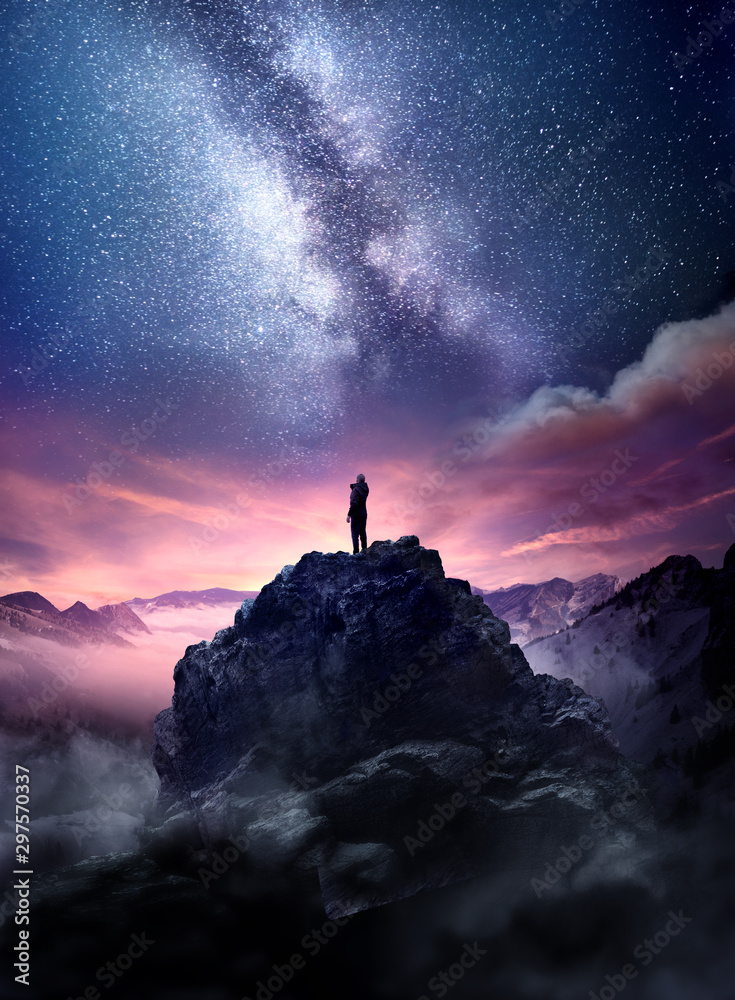 夜空长曝光景观。一名男子站在高高的岩石上，看着星星升到ni中