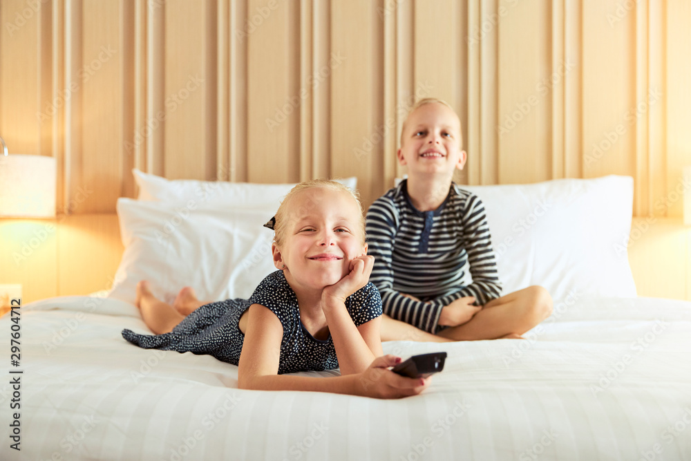 Little girl and her brother watching television on a bed