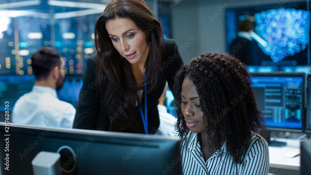 女组长咨询年轻的计算机工程师。她们在神经网络上拥挤的办公室工作