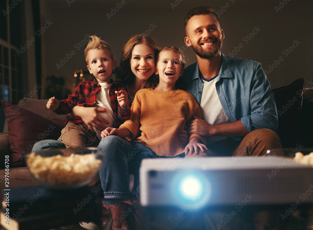 家庭母亲父亲和孩子晚上在家里用爆米花看投影仪、电视、电影