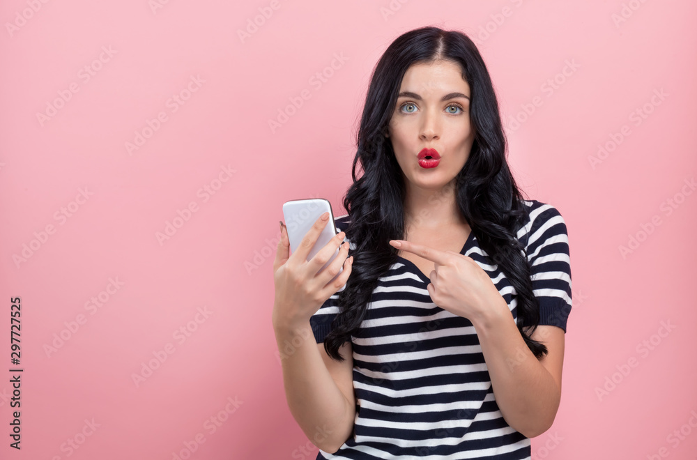 一名年轻女子在粉色背景下手里拿着一部手机