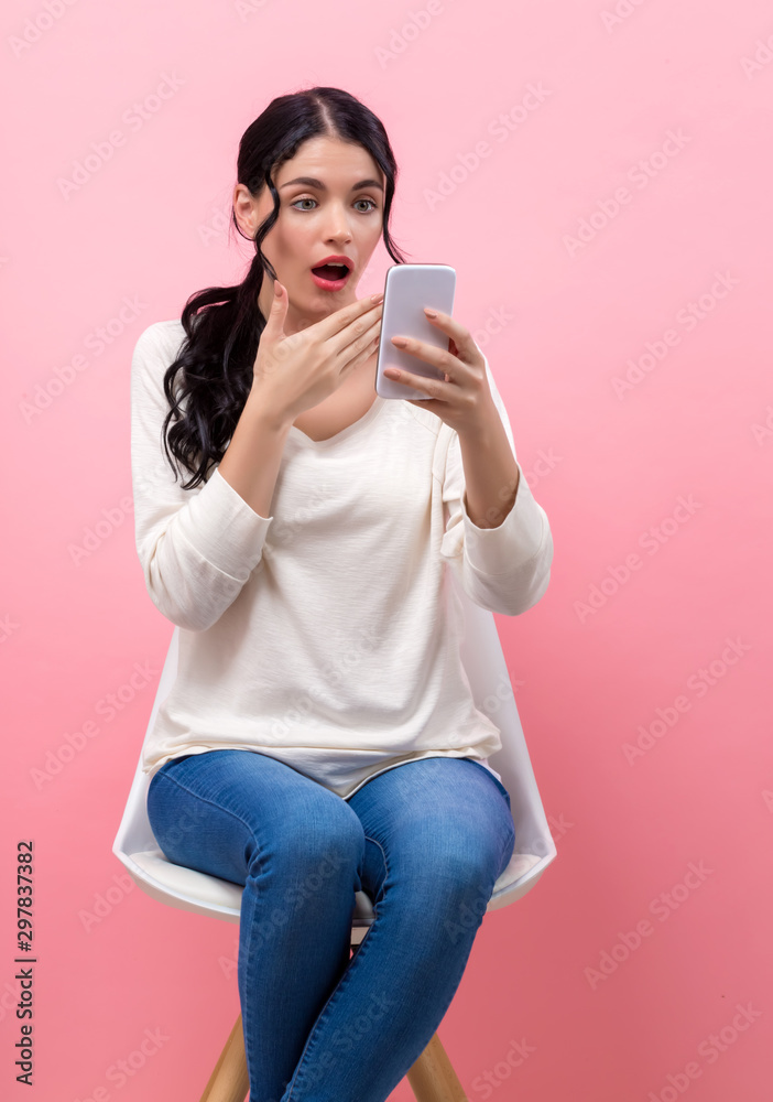 粉红色背景下的年轻女子盯着手机