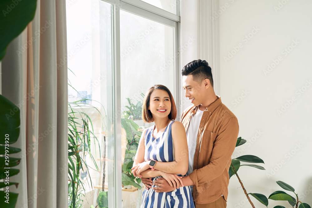幸福的亚洲年轻夫妇在家透过窗户看