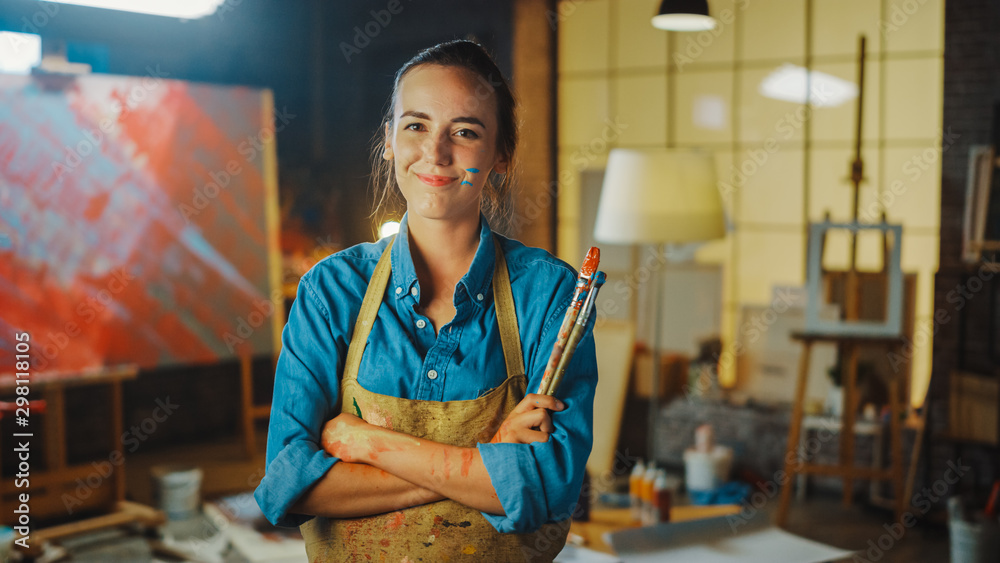 Professional Young Female Artist Dirty with Paint, Wearing Apron, Arms Crossed while Holding Brushes