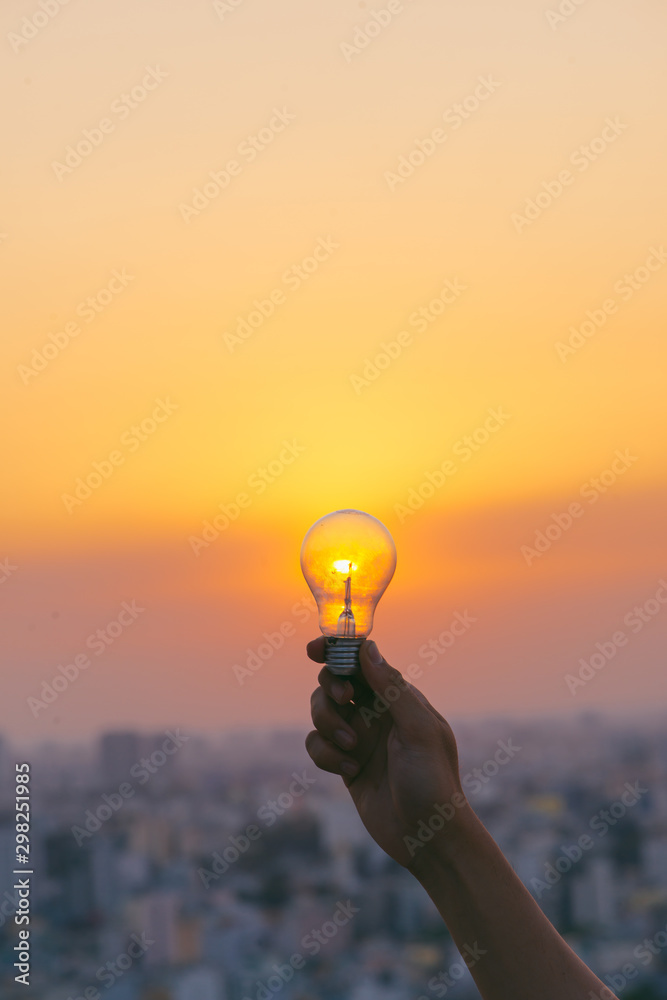 在日落背景下手持灯泡，以节省能源和创意。