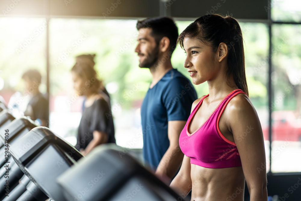 Young fit beautiful Asian woman and handsome Caucasian man walking on treadmill or running machine i