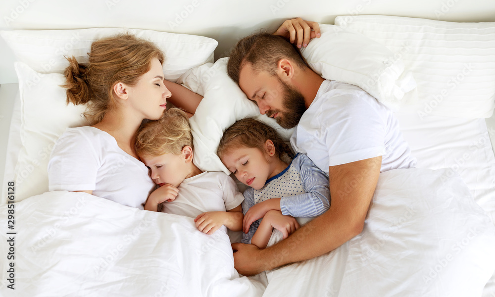 健康的睡眠。幸福的家庭父母和孩子睡在白色的床上