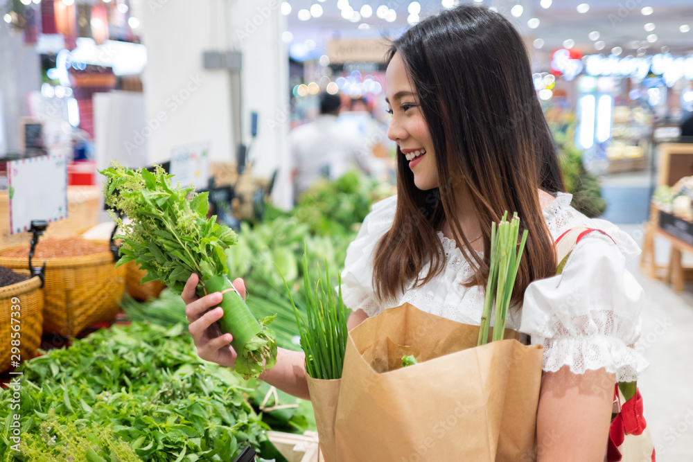 亚洲妇女在超市买蔬菜。她用纸袋和编织袋。为了环境