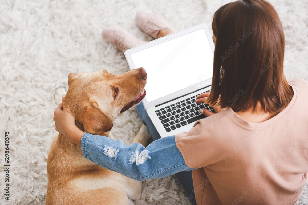 漂亮的年轻女人带着可爱的狗在家里用笔记本电脑