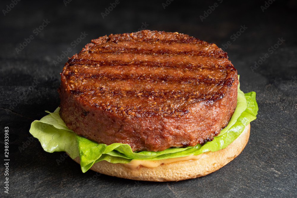 新鲜烤植物汉堡肉饼，面包上有生菜和酱汁，隔离在黑石板上。