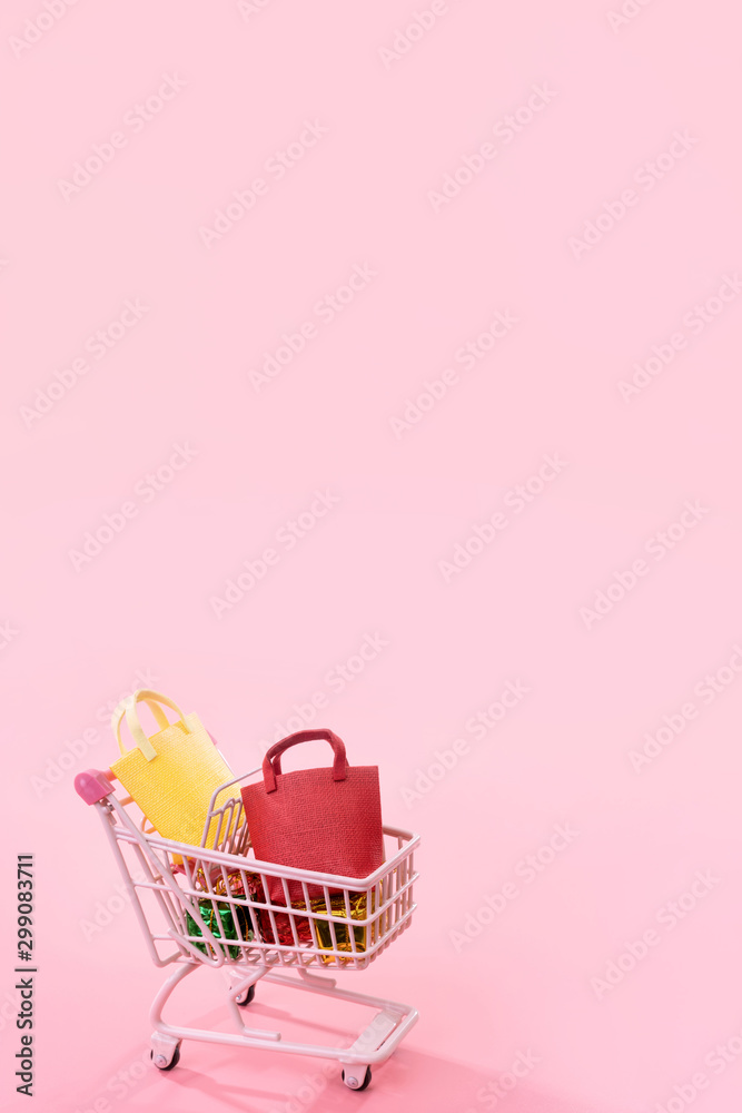 年度大减价购物季概念-迷你粉色购物车手推车，装满纸袋，隔离在上面
