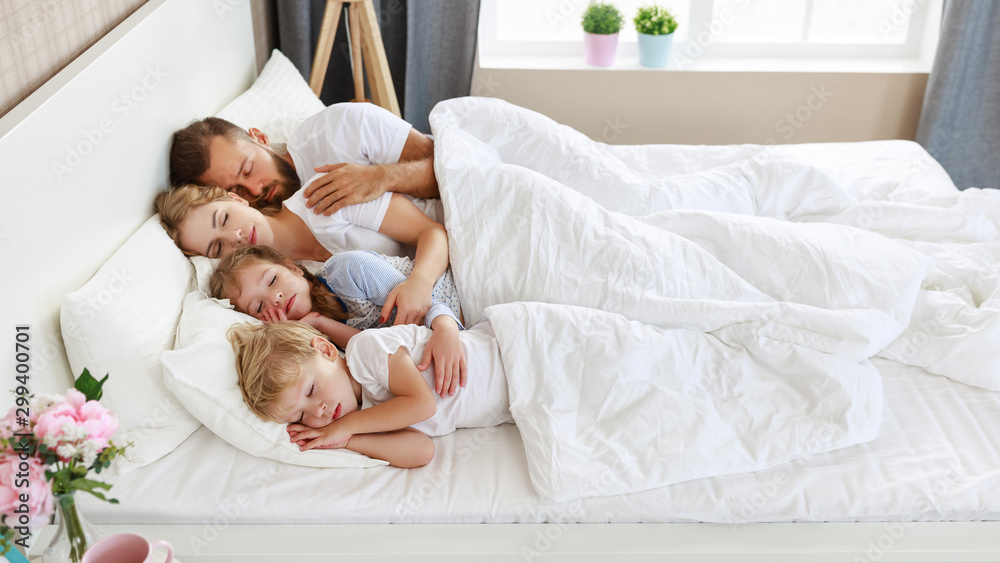 健康的睡眠。幸福的家庭父母和孩子睡在白色的床上。