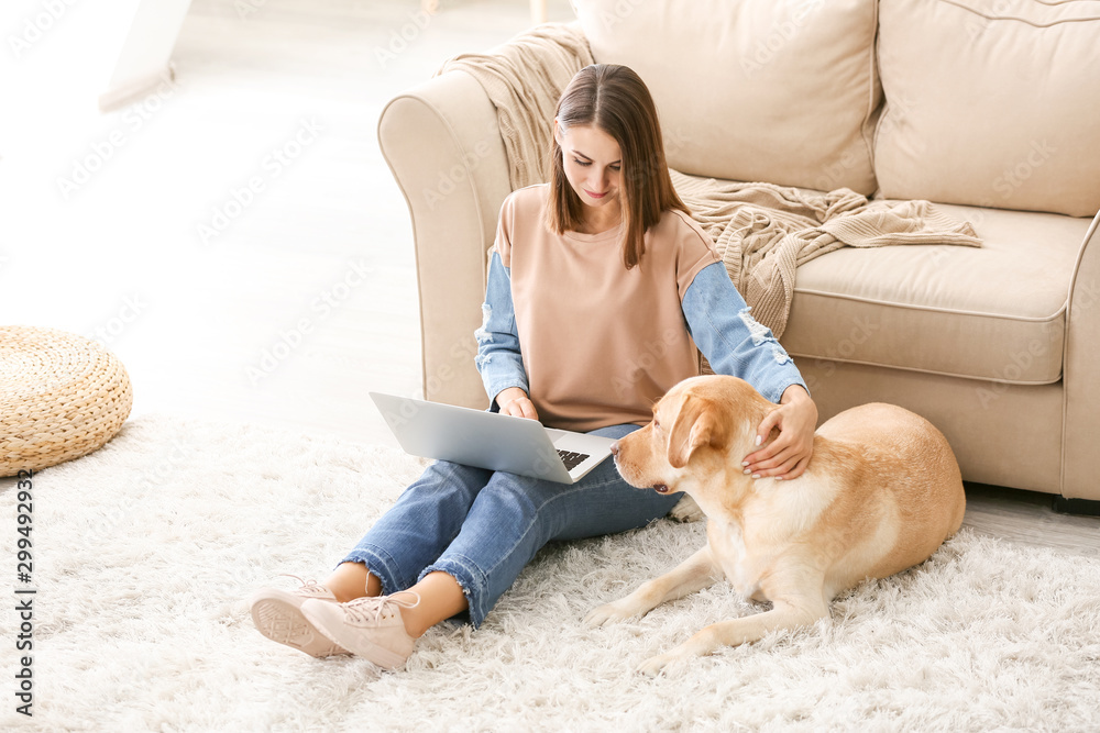 漂亮的年轻女人带着可爱的狗在家里用笔记本电脑
