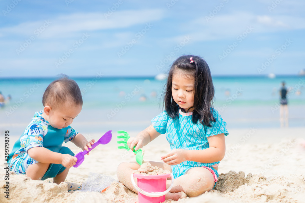 4岁的亚洲小女孩和她1岁的小弟弟在海滩上玩耍。纳图的孩子们