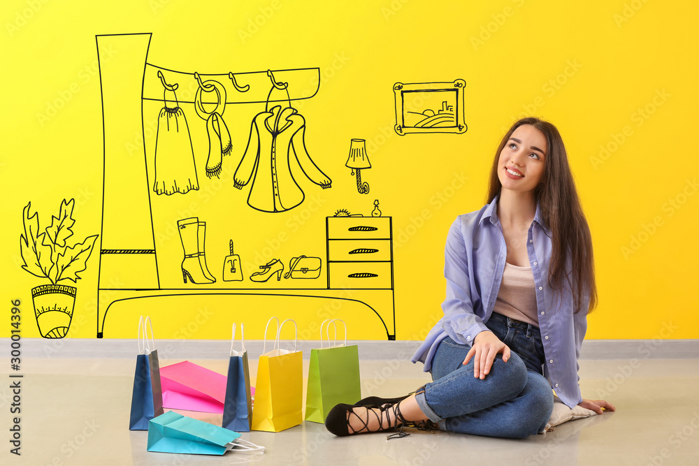 体贴的年轻女人拿着购物袋坐在靠近彩色墙的地板上