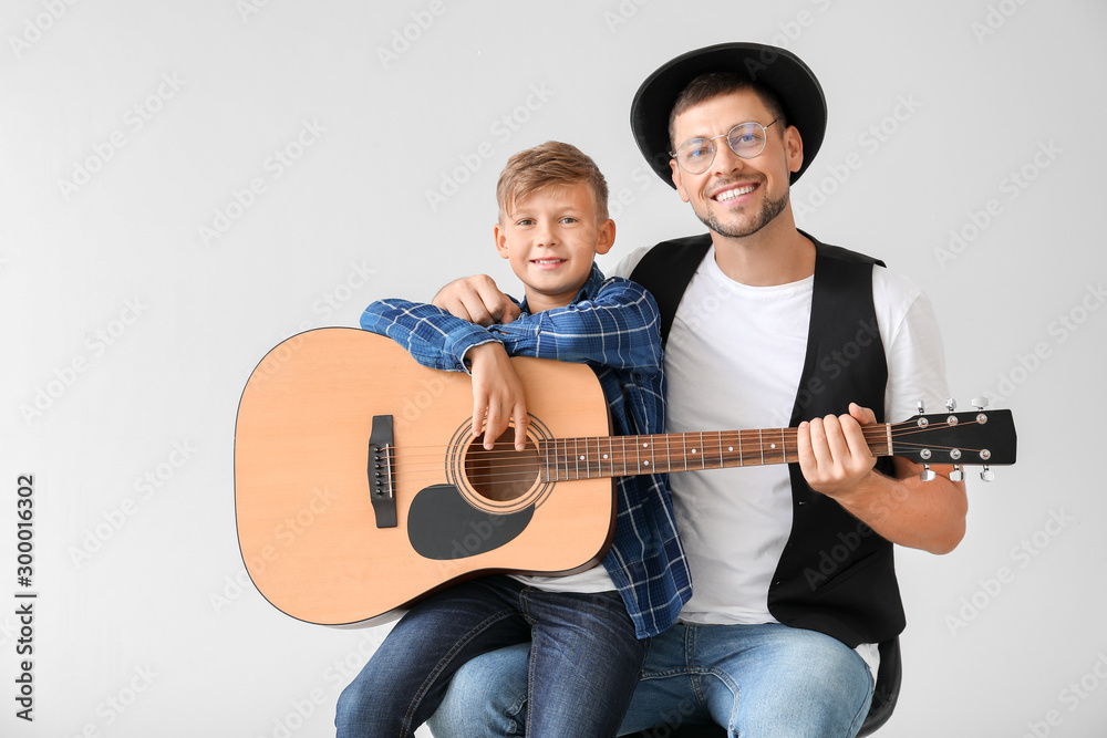 Handsome man and his little son with guitar on light background