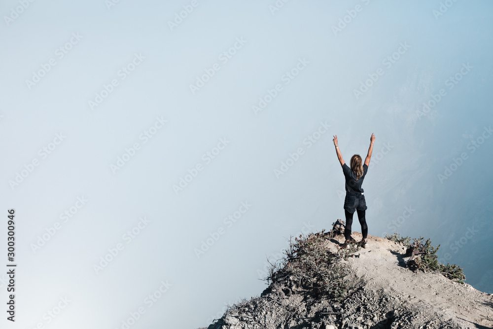 年轻女子在活火山山顶上玩得很开心。站在火山口酸湖上方的高崖上，带着po