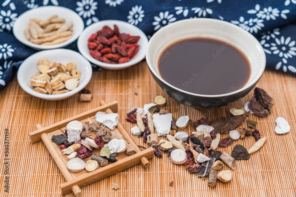 Various Chinese herbal medicines and a bowl of Chinese herbal medicine soup scattered on bamboo mats